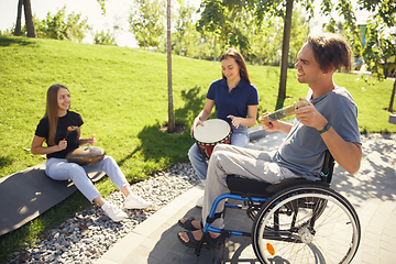 Image showing Happy handicapped man on a wheelchair spending time with friends playing live instrumental music outdoors