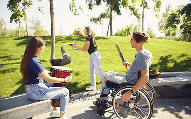 Image showing Happy handicapped man on a wheelchair spending time with friends playing live instrumental music outdoors