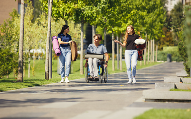 Image showing Happy handicapped man on a wheelchair spending time with friends playing live instrumental music outdoors