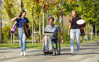 Image showing Happy handicapped man on a wheelchair spending time with friends playing live instrumental music outdoors