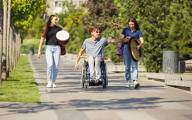 Image showing Happy handicapped man on a wheelchair spending time with friends playing live instrumental music outdoors