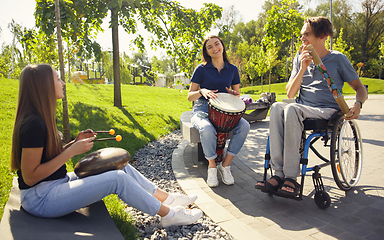 Image showing Happy handicapped man on a wheelchair spending time with friends playing live instrumental music outdoors