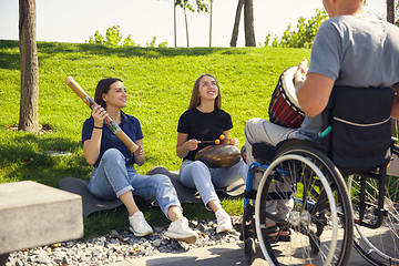 Image showing Happy handicapped man on a wheelchair spending time with friends playing live instrumental music outdoors