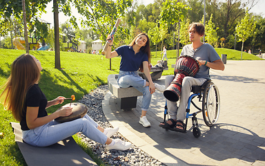 Image showing Happy handicapped man on a wheelchair spending time with friends playing live instrumental music outdoors