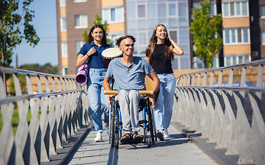 Image showing Happy handicapped man on a wheelchair spending time with friends playing live instrumental music outdoors