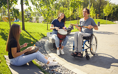 Image showing Happy handicapped man on a wheelchair spending time with friends playing live instrumental music outdoors