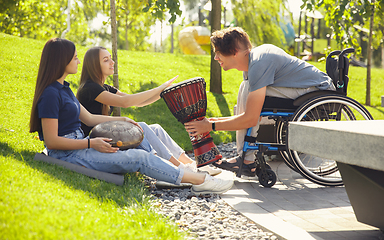 Image showing Happy handicapped man on a wheelchair spending time with friends playing live instrumental music outdoors