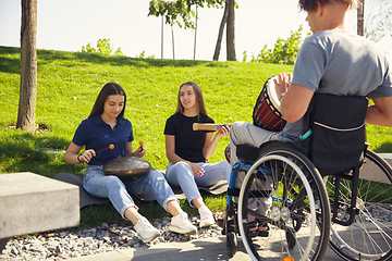 Image showing Happy handicapped man on a wheelchair spending time with friends playing live instrumental music outdoors