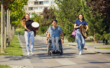 Image showing Happy handicapped man on a wheelchair spending time with friends playing live instrumental music outdoors