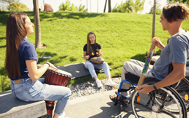 Image showing Happy handicapped man on a wheelchair spending time with friends playing live instrumental music outdoors