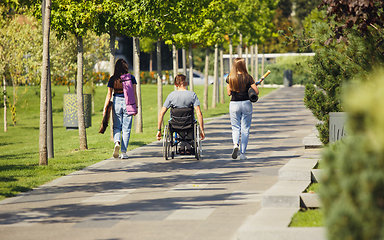 Image showing Happy handicapped man on a wheelchair spending time with friends playing live instrumental music outdoors