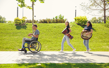 Image showing Happy handicapped man on a wheelchair spending time with friends playing live instrumental music outdoors