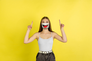 Image showing Portrait of young girl with emotion on her protective face mask isolated on studio background. Beautiful female model, funny expression