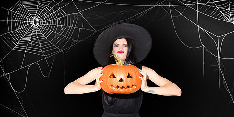 Image showing Young woman in hat as a witch on scary black background