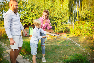 Image showing Happy family during watering plants in a garden outdoors. Love, family, lifestyle, harvest concept.