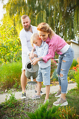 Image showing Happy family during watering plants in a garden outdoors. Love, family, lifestyle, harvest concept.