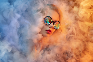Image showing Young beautiful woman on neon colored studio background in smoke cloud. Human emotions, facial expression, beauty concept.