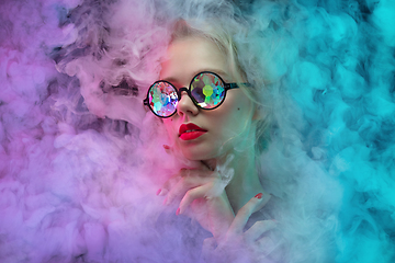 Image showing Young beautiful woman on neon colored studio background in smoke cloud. Human emotions, facial expression, beauty concept.