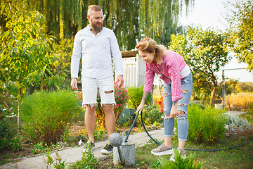 Image showing Happy family during watering plants in a garden outdoors. Love, family, lifestyle, harvest concept.