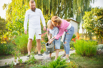 Image showing Happy family during watering plants in a garden outdoors. Love, family, lifestyle, harvest concept.