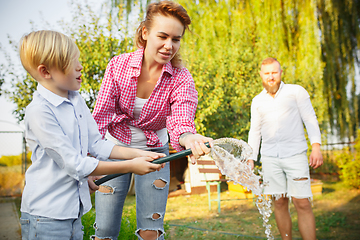 Image showing Happy family during watering plants in a garden outdoors. Love, family, lifestyle, harvest concept.