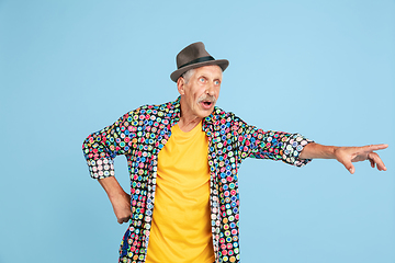 Image showing Senior hipster man in stylish hat isolated on blue background. Tech and joyful elderly lifestyle concept