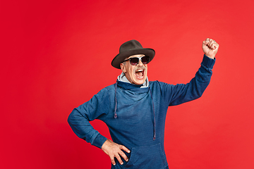 Image showing Senior man in stylish eyewear and hat isolated on red background. Tech and joyful elderly lifestyle concept