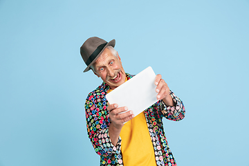 Image showing Senior hipster man in stylish hat isolated on blue background. Tech and joyful elderly lifestyle concept