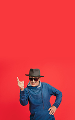 Image showing Senior man in stylish eyewear and hat isolated on red background. Tech and joyful elderly lifestyle concept