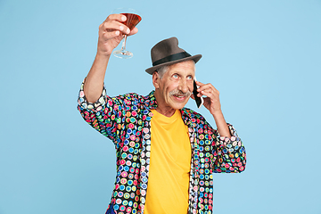 Image showing Senior hipster man in stylish hat isolated on blue background. Tech and joyful elderly lifestyle concept