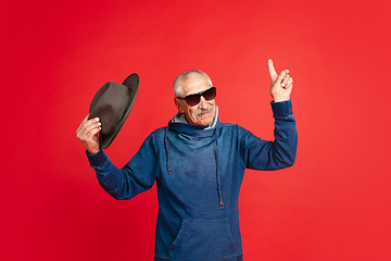Image showing Senior man in stylish eyewear and hat isolated on red background. Tech and joyful elderly lifestyle concept