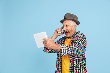 Image showing Senior hipster man in stylish hat isolated on blue background. Tech and joyful elderly lifestyle concept