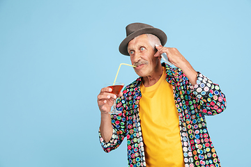 Image showing Senior hipster man in stylish hat isolated on blue background. Tech and joyful elderly lifestyle concept