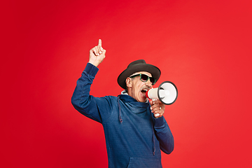 Image showing Senior man in stylish eyewear and hat isolated on red background. Tech and joyful elderly lifestyle concept