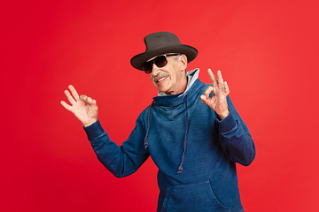 Image showing Senior man in stylish eyewear and hat isolated on red background. Tech and joyful elderly lifestyle concept