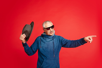 Image showing Senior man in stylish eyewear and hat isolated on red background. Tech and joyful elderly lifestyle concept