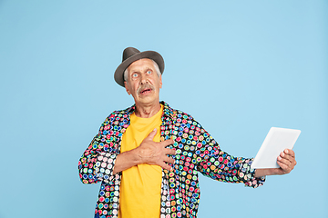 Image showing Senior hipster man in stylish hat isolated on blue background. Tech and joyful elderly lifestyle concept