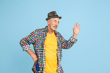 Image showing Senior hipster man in stylish hat isolated on blue background. Tech and joyful elderly lifestyle concept