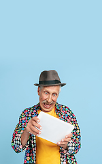 Image showing Senior hipster man in stylish hat isolated on blue background. Tech and joyful elderly lifestyle concept