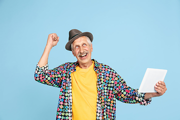 Image showing Senior hipster man in stylish hat isolated on blue background. Tech and joyful elderly lifestyle concept