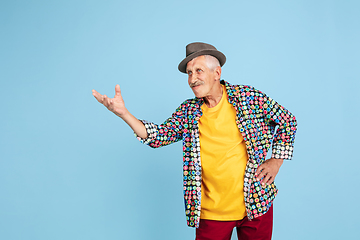 Image showing Senior hipster man in stylish hat isolated on blue background. Tech and joyful elderly lifestyle concept