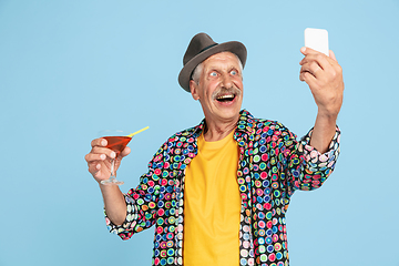 Image showing Senior hipster man in stylish hat isolated on blue background. Tech and joyful elderly lifestyle concept