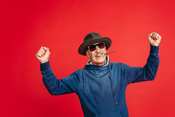 Image showing Senior man in stylish eyewear and hat isolated on red background. Tech and joyful elderly lifestyle concept