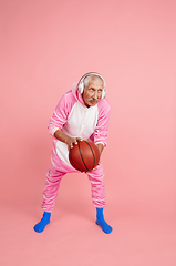 Image showing Senior hipster man in stylish pink attire isolated on pink background. Tech and joyful elderly lifestyle concept