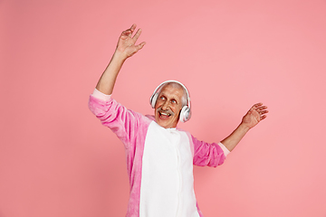 Image showing Senior hipster man in stylish pink attire isolated on pink background. Tech and joyful elderly lifestyle concept