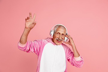 Image showing Senior hipster man in stylish pink attire isolated on pink background. Tech and joyful elderly lifestyle concept