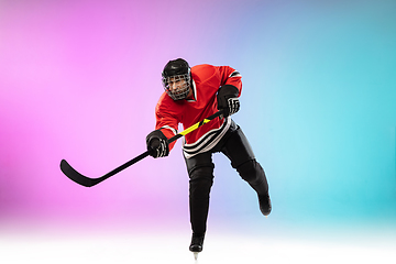 Image showing Male hockey player with the stick on ice court and neon colored gradient background. Sportsman wearing equipment, helmet practicing.