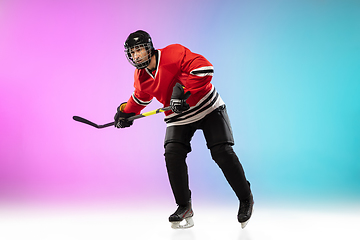 Image showing Male hockey player with the stick on ice court and neon colored gradient background. Sportsman wearing equipment, helmet practicing.