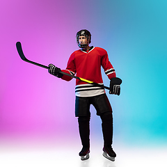 Image showing Male hockey player with the stick on ice court and neon colored gradient background. Sportsman wearing equipment, helmet practicing.