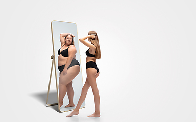 Image showing Young slim woman looking at fat girl in mirror\'s reflection on white background